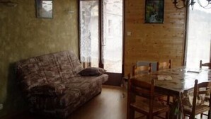 A room with a patterned sofa, a wooden dining table with chairs, and a large window with a view.