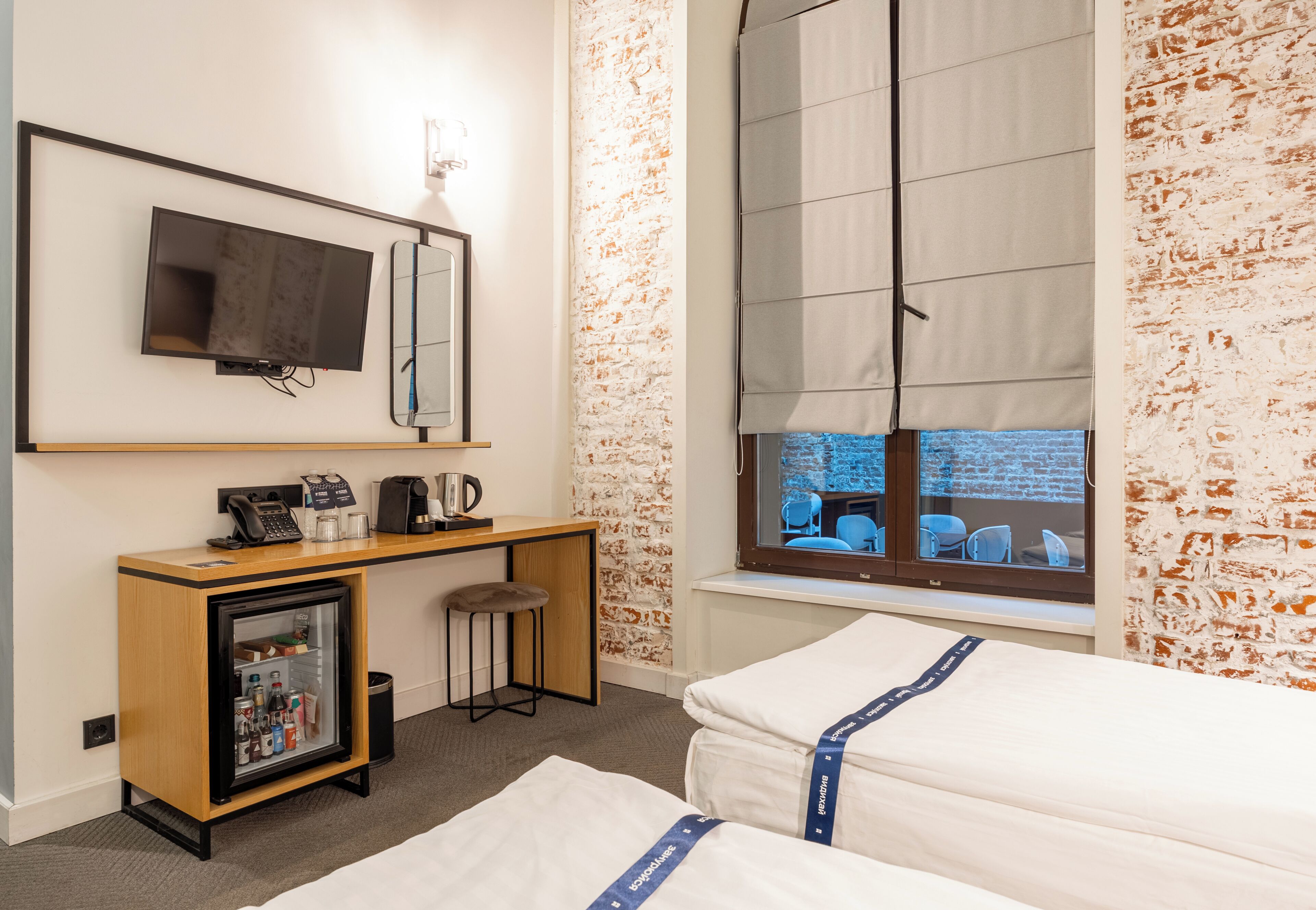 A hotel room with a bed, a desk with a computer, a refrigerator, a window with a view, and a television mounted on the wall.