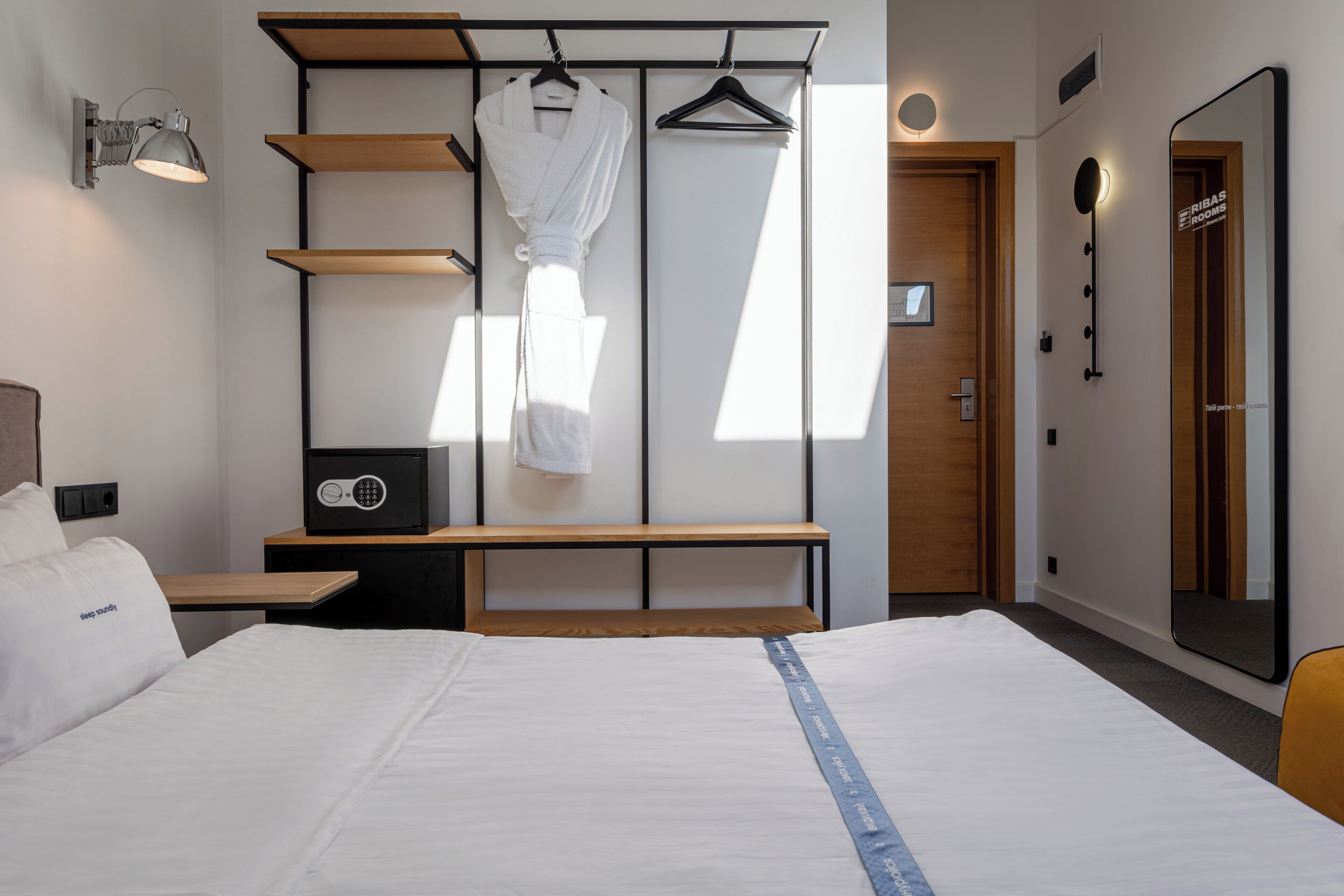 Una camera d'albergo con un letto, una panca, un accappatoio e uno specchio.
