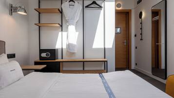 Una camera d'albergo con un letto, una panca, un accappatoio e uno specchio.