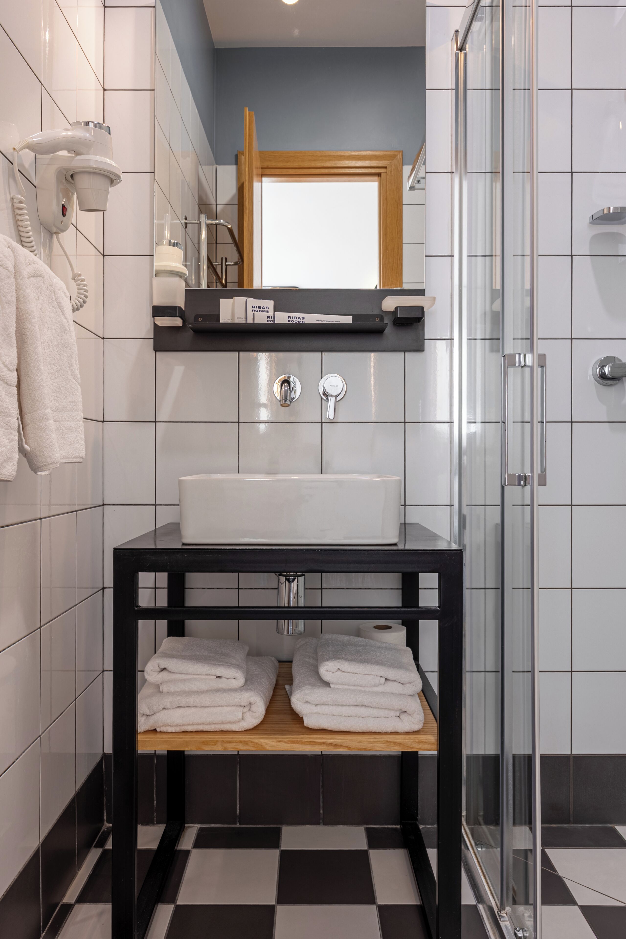 Une salle de bain avec un lavabo blanc, un meuble-lavabo noir et une cabine de douche en verre.