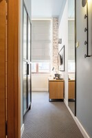 Un pasillo con un armario de madera, un escritorio con una lámpara, un espejo y una lámpara de pared.