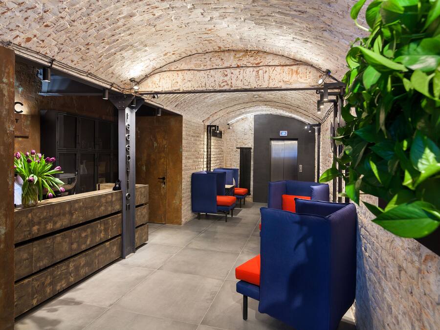 A modern lobby with a brick ceiling, wooden reception desk, blue seating, and a plant.