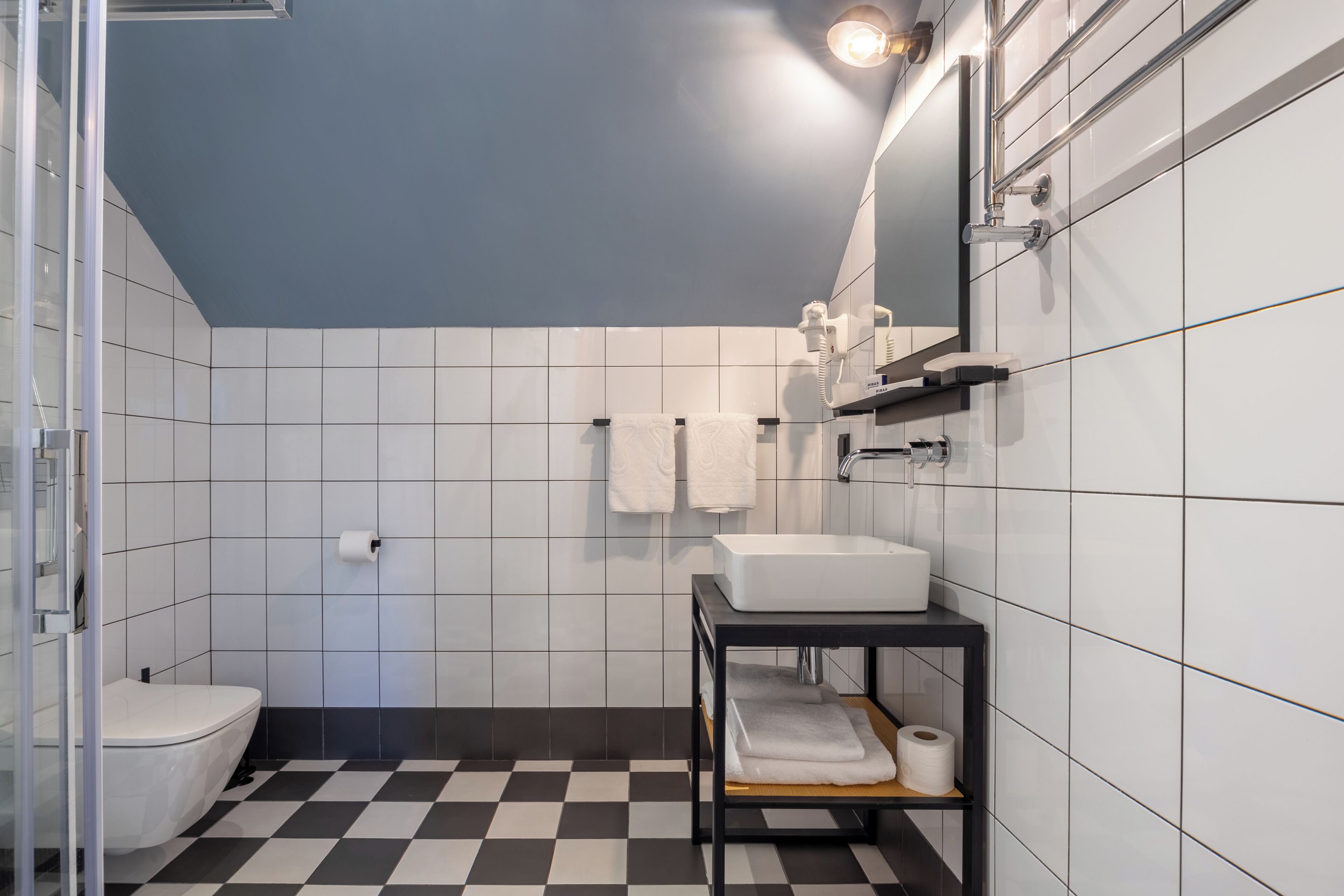 A modern bathroom with a checkered floor, white tiles, a white sink, a toilet, and a mirror.