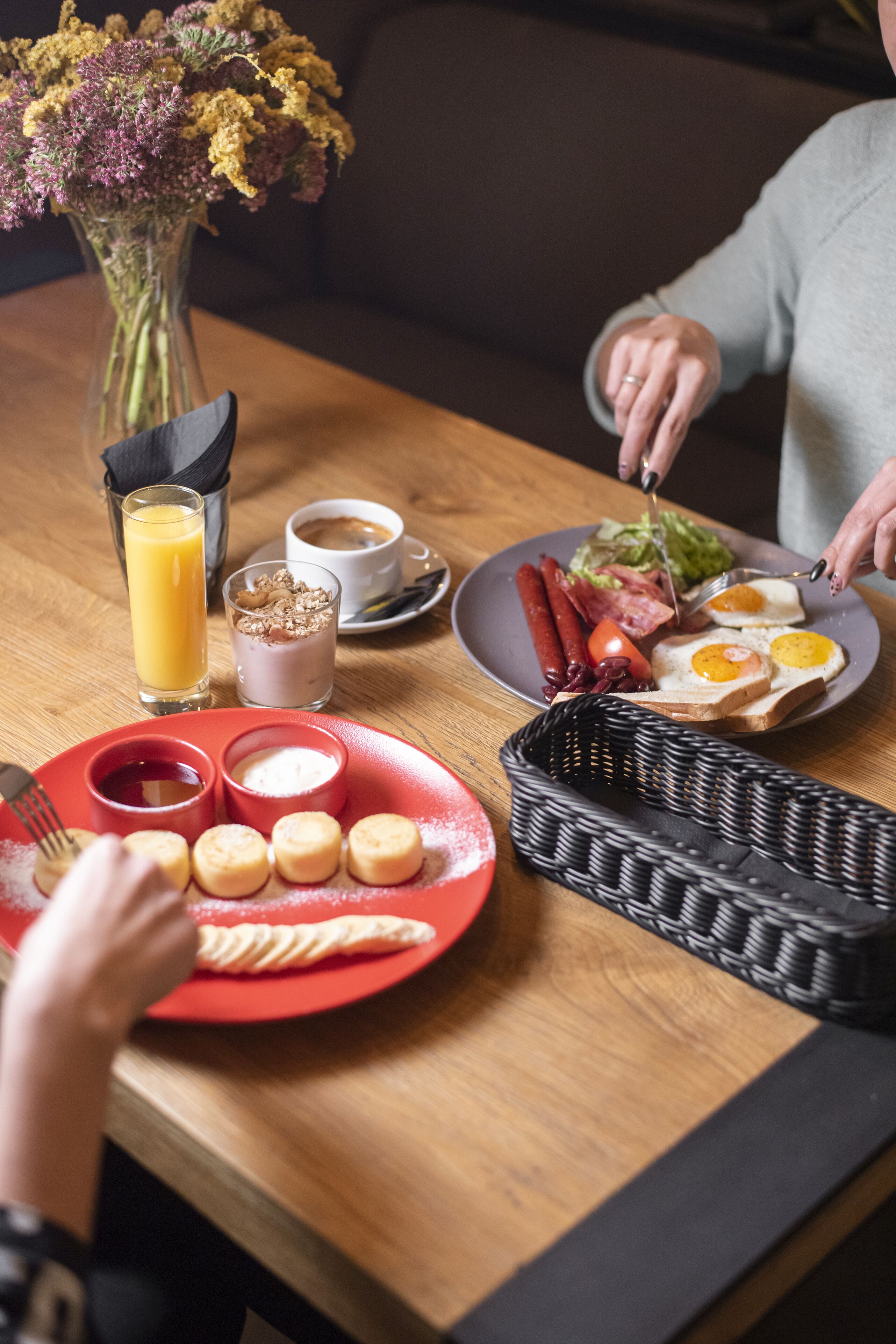 A breakfast setting with a plate of eggs, sausages, and toast, a glass of orange juice, and a vase of flowers.