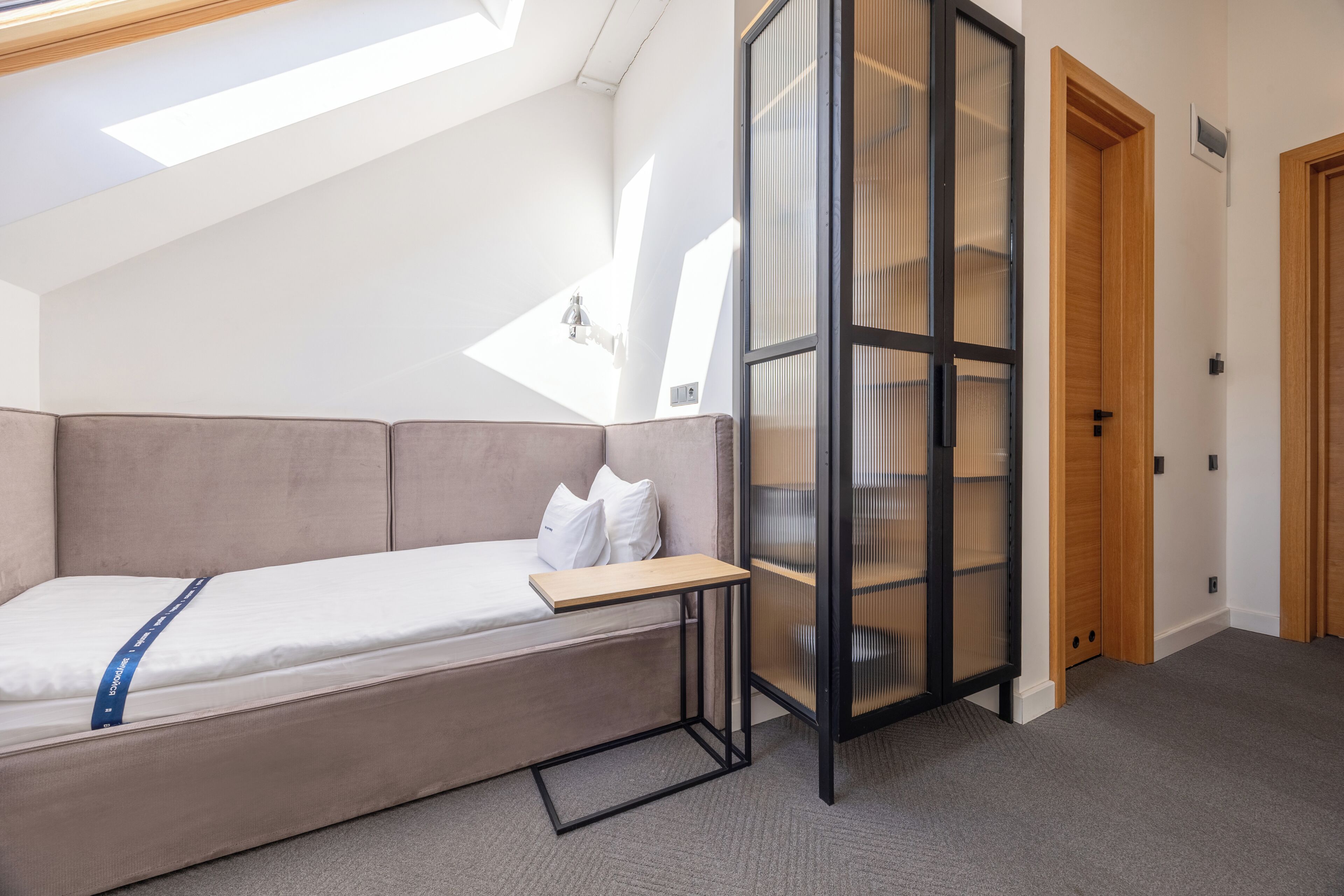 A loft-style bedroom with a bed, a small table, a glass partition, and a skylight.