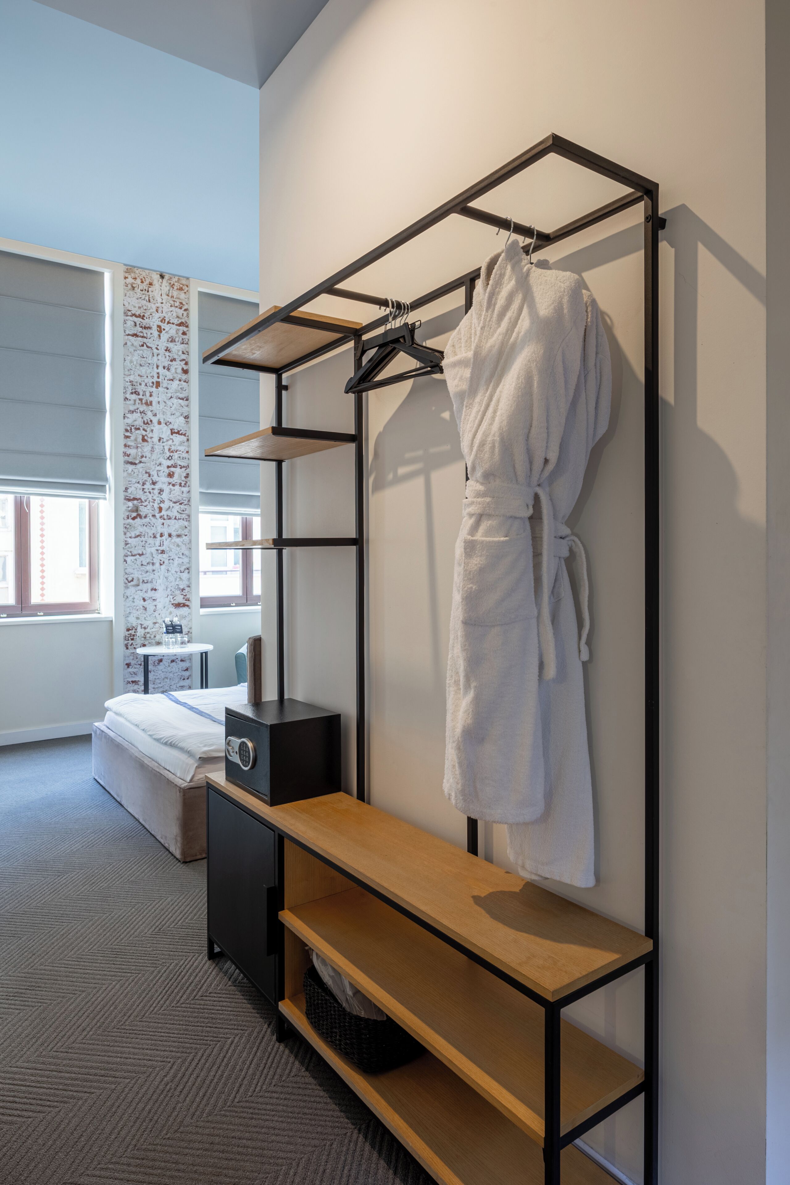 A modern hotel room with a bed, a wooden bench, a robe rack, and a small table with a radio.