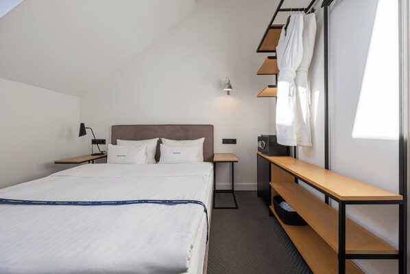 A hotel room with a bed, bedside tables, a desk, a bench, and a hanging robe rack. - FERENC Hotel & Restaurant (Lviv)