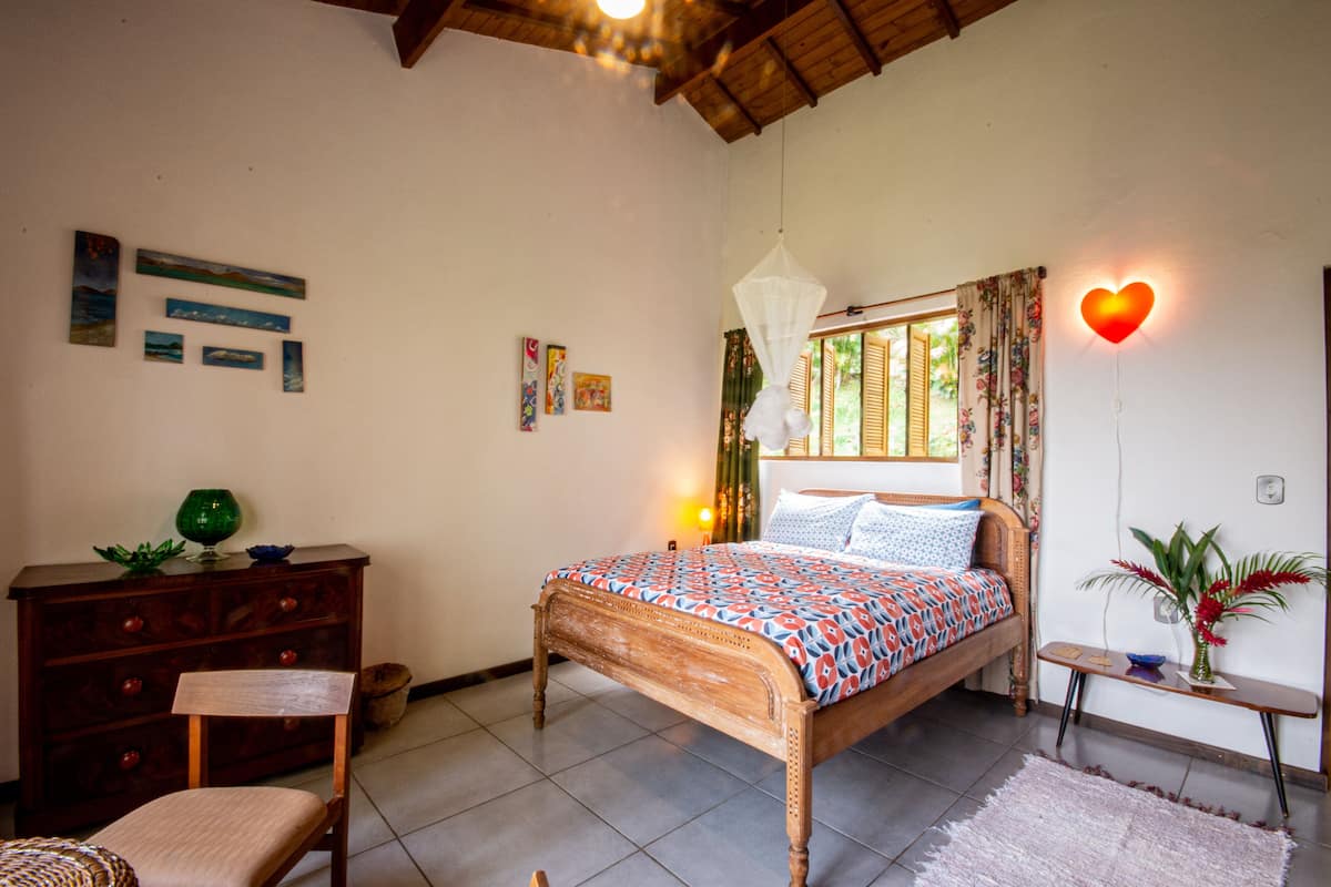 A bedroom with a wooden bed, a nightstand, a dresser, a chair, and a window with curtains.