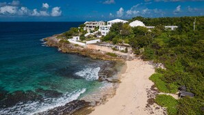 Propiedad costera con playa, vista al océano y varias construcciones rodeadas de follaje.
