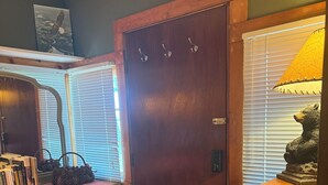 Una habitación con un aparador de madera, una mesita con lámpara y una puerta con ganchos.