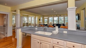 A spacious kitchen with a large island, white cabinetry, and a view to the dining area. - Large home with private guest crofter across from the beach access, wrap around porches (Bald Head Island)