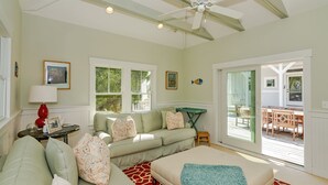 A spacious living room with a large couch, a coffee table, and a sofa. There is a ceiling fan, a window with a view of the outdoors, and a sliding glass door leading to a patio area. - Large home with private guest crofter across from the beach access, wrap around porches (Bald Head Island)