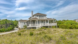 A large, two-story house with a balcony and a covered porch, surrounded by natural vegetation. - Large home with private guest crofter across from the beach access, wrap around porches (Bald Head Island)