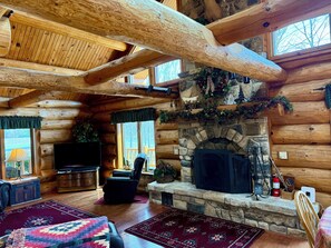 A log cabin interior with a stone fireplace, wooden beams, a television, and a cozy seating area.