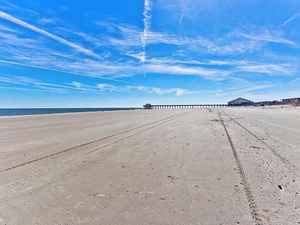 Una playa con un muelle que se adentra en el agua, una zona techada y un cielo despejado.