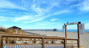 Une plage avec une promenade en bois menant à une jetée. Un panneau indique « 17th Street » et énumère les règles à respecter sur la plage.