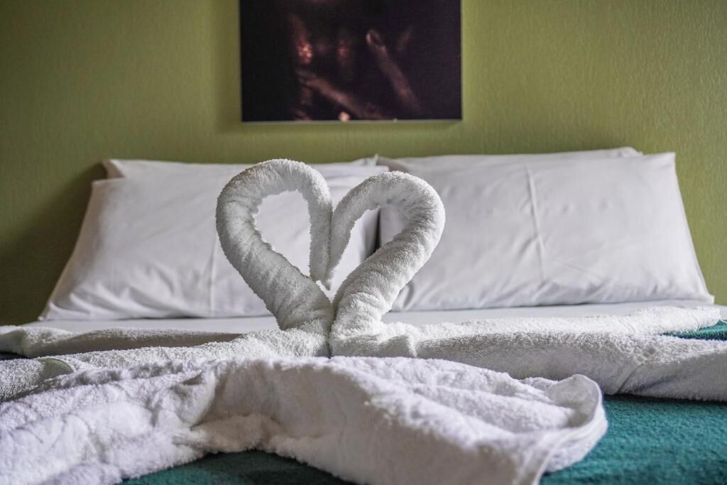 A bed with white pillows and a blanket, and a towel arranged in a heart shape on the bed.