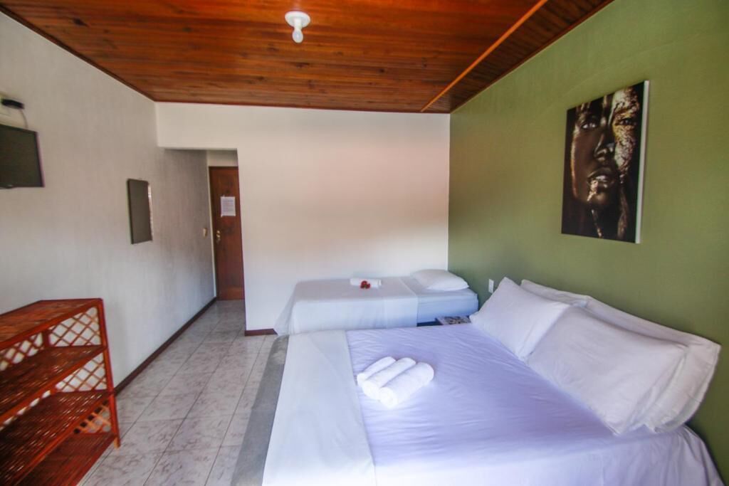 A hotel room with two beds, a wooden ceiling, a green wall, and a painting.