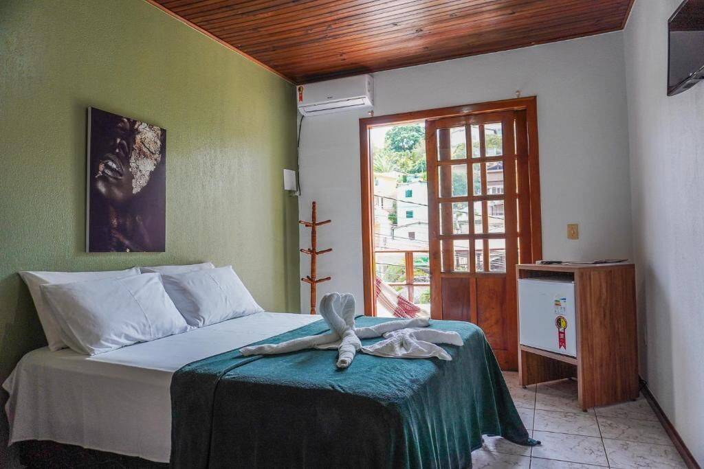 A hotel room with a bed, a green wall, a wooden ceiling, a door with glass panels, and a small wooden cabinet.