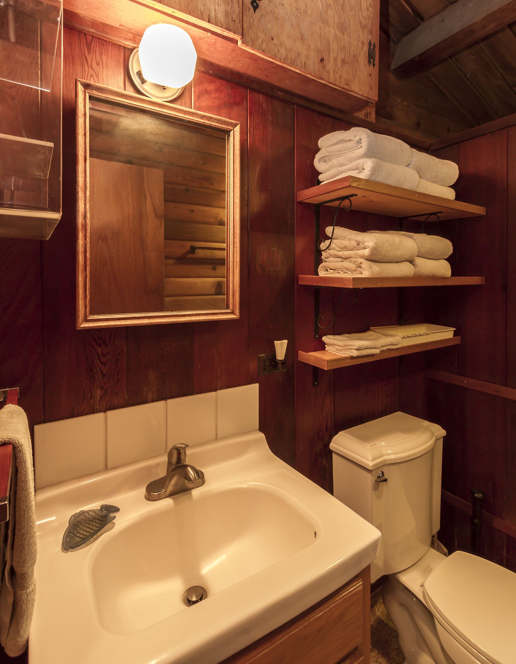 Ein Badezimmer aus Holz mit Waschbecken, Spiegel und gestapelten Handtüchern.