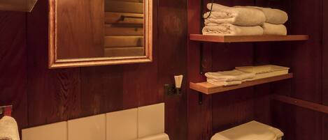 Ein Badezimmer aus Holz mit Waschbecken, Spiegel und gestapelten Handtüchern.