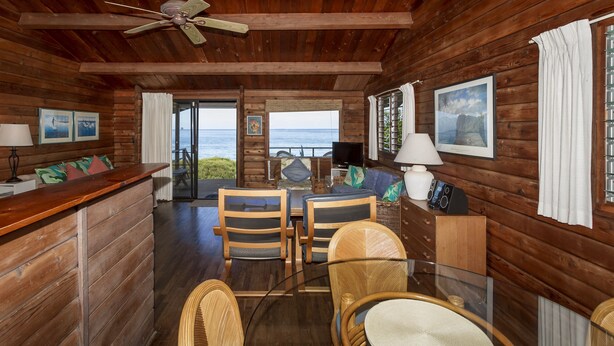 A wooden cabin with a dining area, a television, and a view of the ocean. - Beachfront Cottage at Log Cabins (Haleiwa)