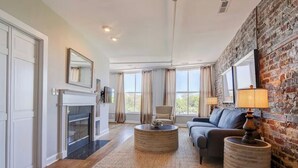 A living room with a fireplace, a sofa, a coffee table, and a brick wall. - The Soho Suite - Where Luxury & Location Meet (Charleston)