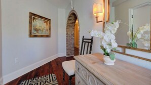 A hallway with a wooden floor, a bench, a dresser, a mirror, and a wall-mounted light fixture. - The Soho Suite - Where Luxury & Location Meet (Charleston)