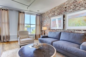 A living room with a brick wall, a sofa, a chair, and a round coffee table.