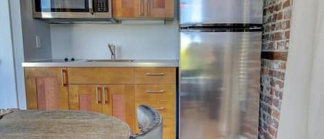 Une cuisine compacte équipée d’un réfrigérateur en acier inoxydable, d’un four à micro-ondes, de meubles de rangement en bois et d’une table ronde.