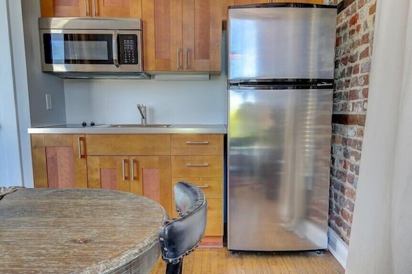 A compact kitchen with a stainless steel refrigerator, a microwave, wooden cabinets, and a round table.