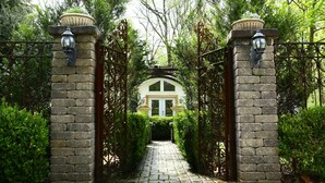 Un arco de piedra que conduce a un edificio con fachada blanca y techo verde, rodeado de abundante vegetación.
