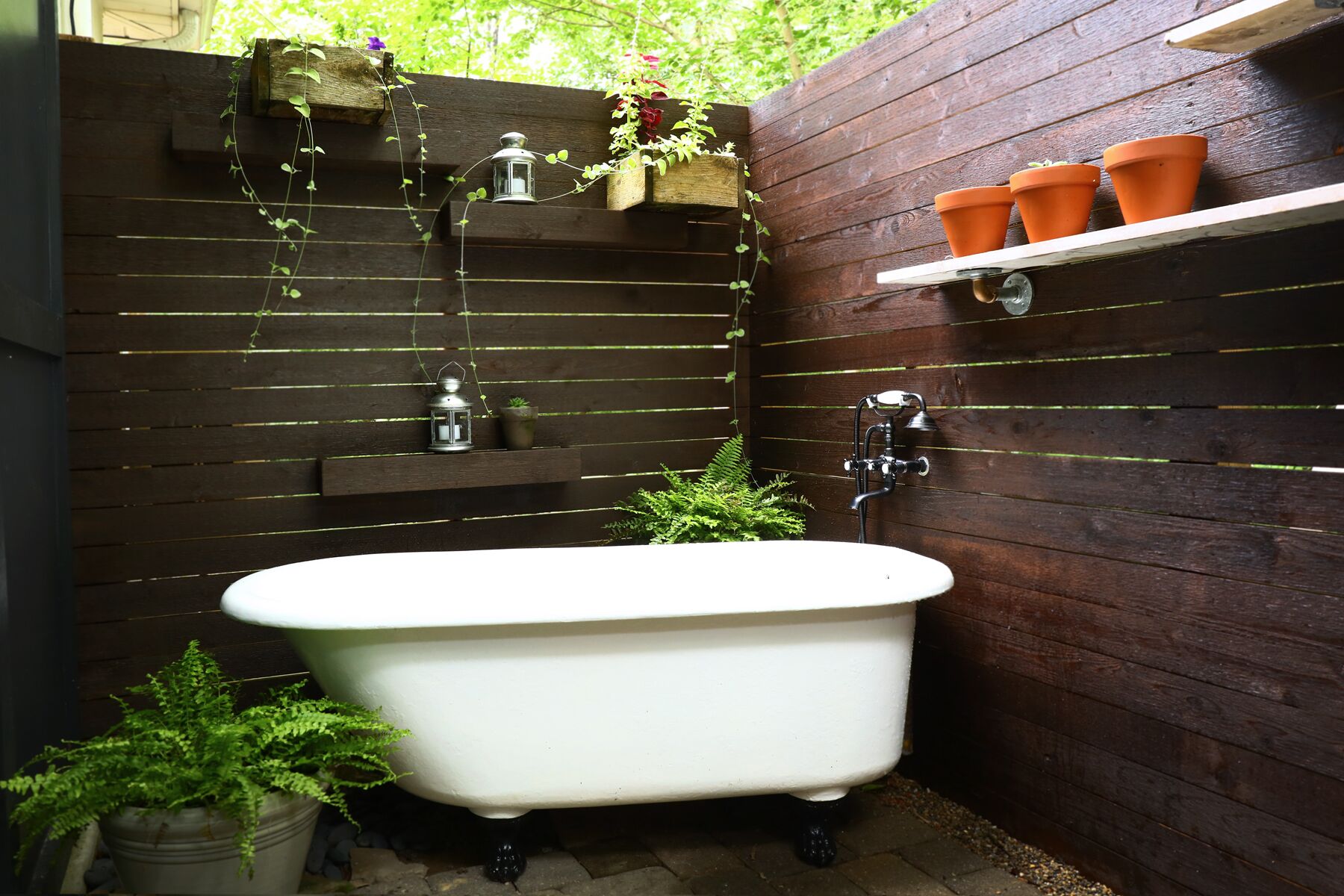 Une salle de bain avec une baignoire sur pieds blanche, des étagères en bois ornées de plantes et une petite étagère avec des pots en terre cuite.