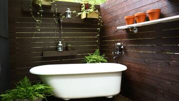 Une salle de bain avec une baignoire sur pieds blanche, des étagères en bois ornées de plantes et une petite étagère avec des pots en terre cuite.