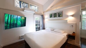 Un dormitorio moderno con una cama grande, un televisor instalado en la pared y una ventana con vistas a árboles.