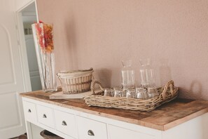 A wooden counter with a wicker basket holding several clear glasses and a woven basket with a cloth.