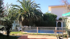 A pool area with a fenced patio, palm trees, and a building in the background. - Hotel Genova (Los Andes)