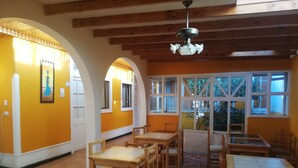 A dining area with wooden tables and chairs, a ceiling fan, and large windows with views of greenery. - Hotel Genova (Los Andes)