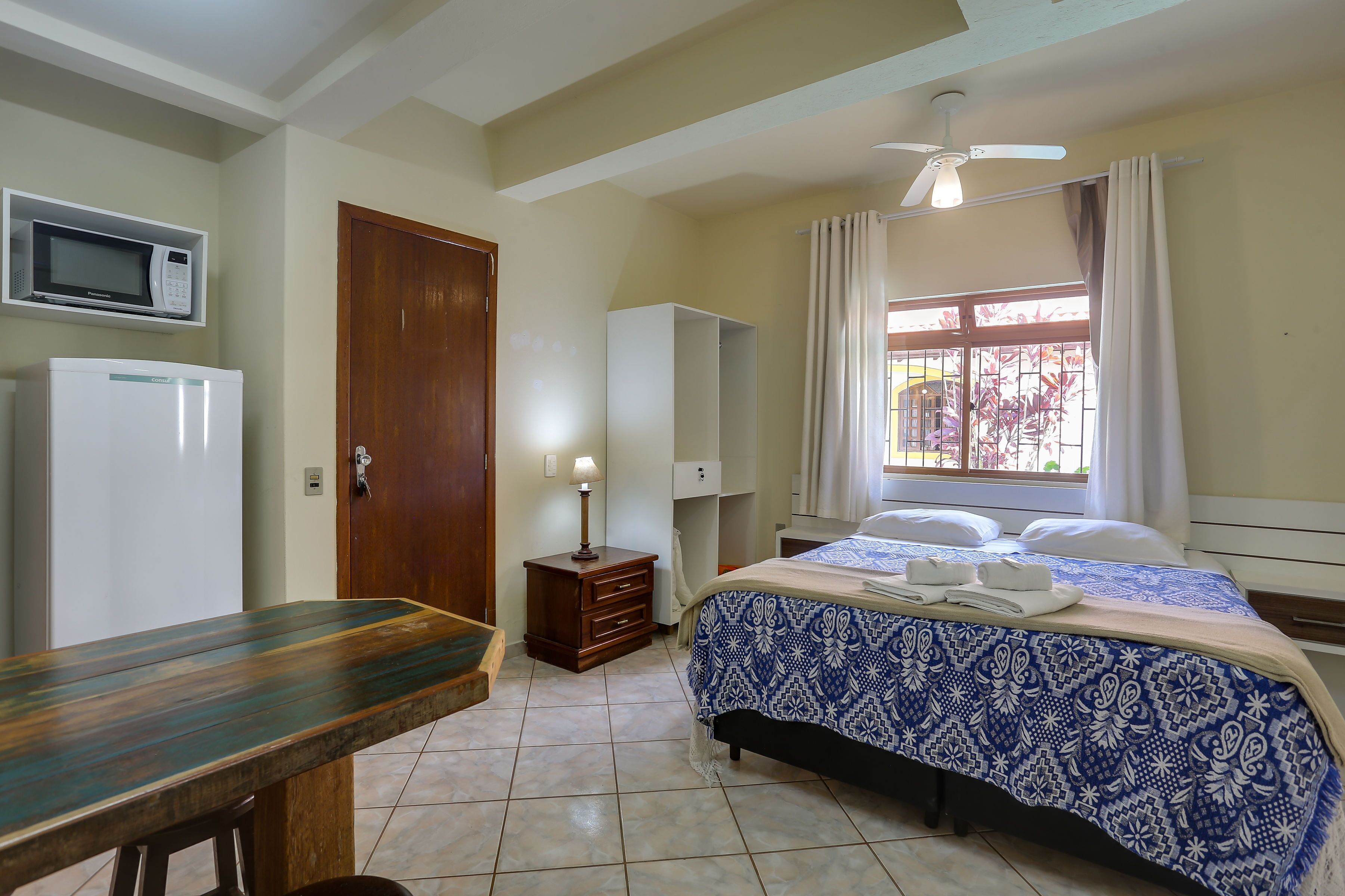 A bedroom with a bed, a desk, a microwave, a wardrobe, and a ceiling fan.