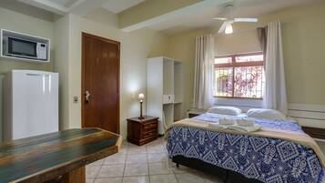 A bedroom with a bed, a desk, a microwave, a wardrobe, and a ceiling fan.