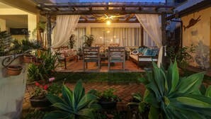 Un espacio de estar al aire libre cubierto con una pérgola, sillas acolchadas y una mesa de comedor.