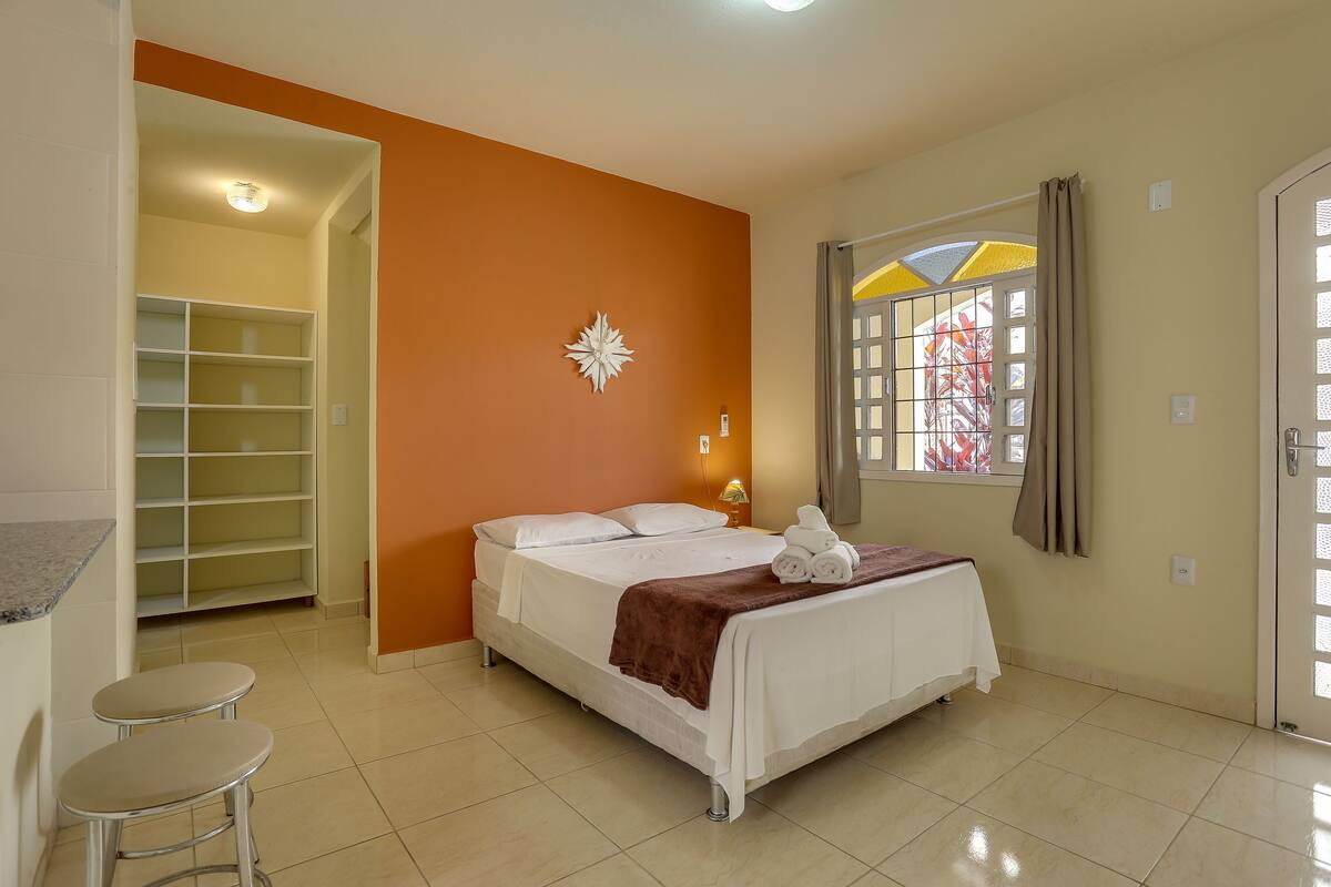 A bedroom with a bed, a nightstand, a shelf, and a window with curtains.