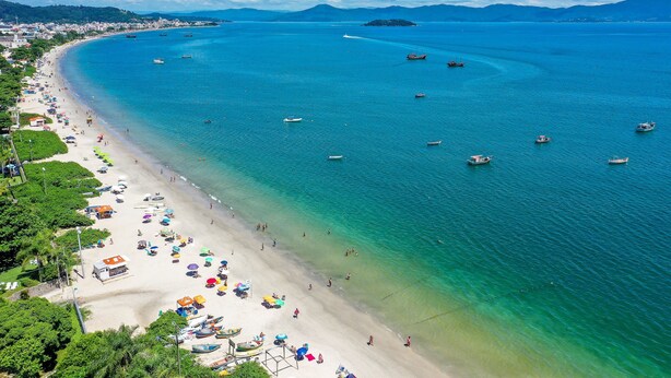 Una playa costera con aguas turquesas cristalinas, embarcaciones y sombrillas.