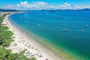 Una playa costera con aguas turquesas cristalinas, embarcaciones y sombrillas.