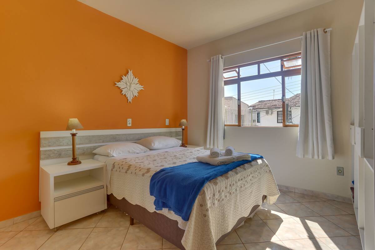 A bedroom with a bed, nightstands, a window with curtains, and a decorative wall piece.