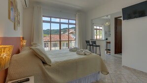 Habitación de hotel con una cama grande, un escritorio con dos sillas y vistas a la ciudad a través de amplios ventanales.