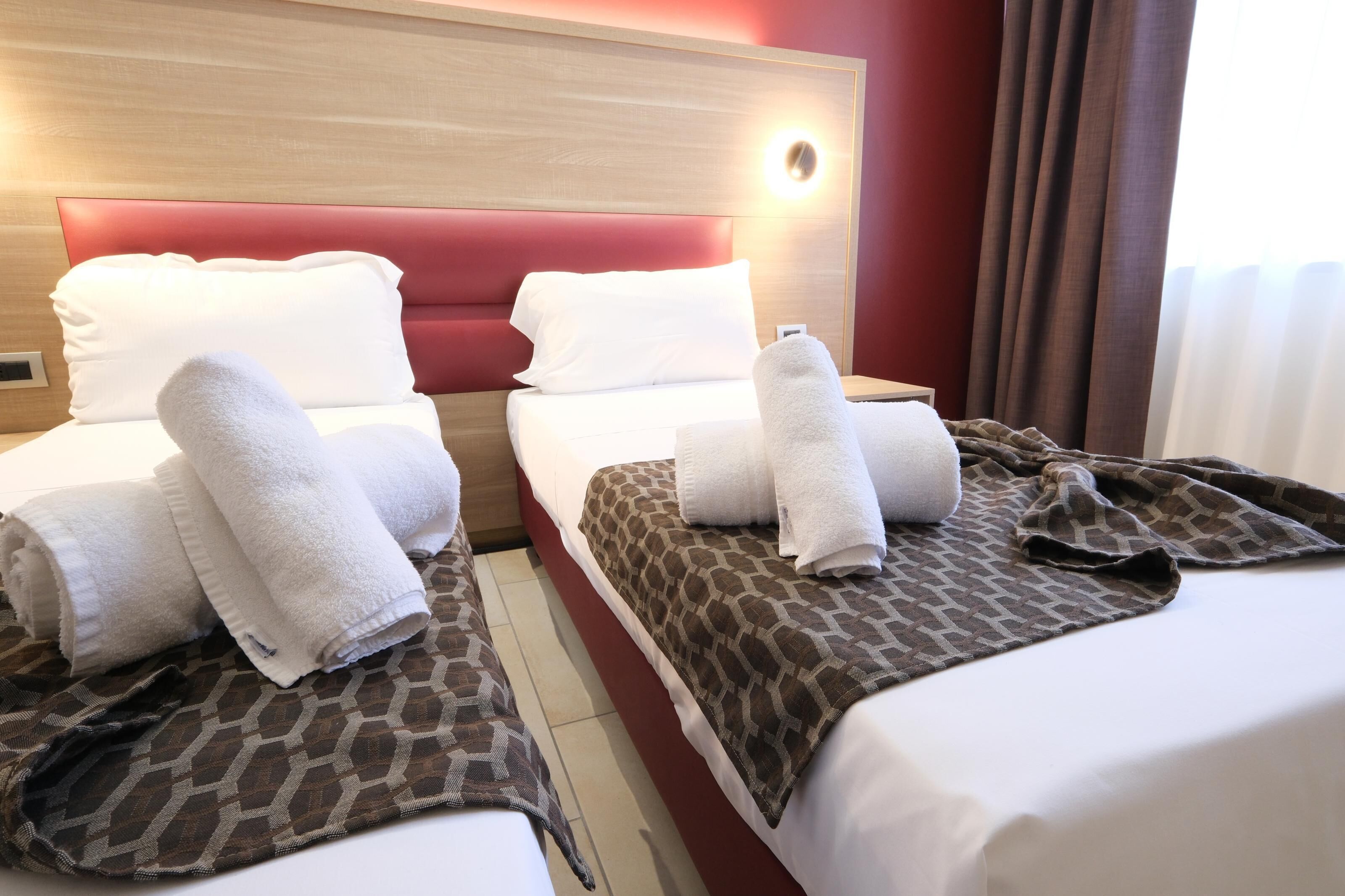Two beds with white and patterned bedspreads, a red headboard, and a wall-mounted light.