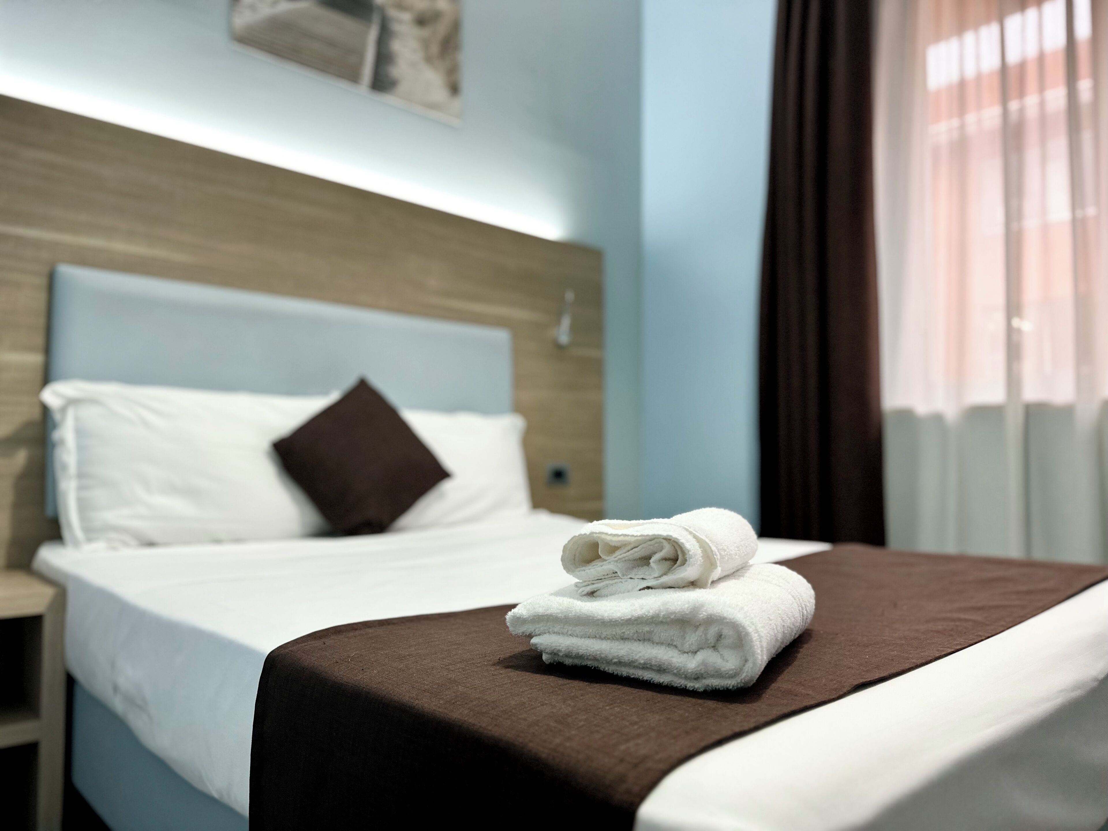 A neatly made bed with a brown headboard, white pillows, and a folded white towel on the bed.
