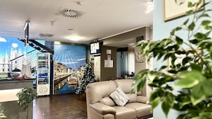 Un vestíbulo de hotel con un gran mural de un paisaje urbano, un sofá de cuero, un árbol de Navidad y una nevera pequeña.